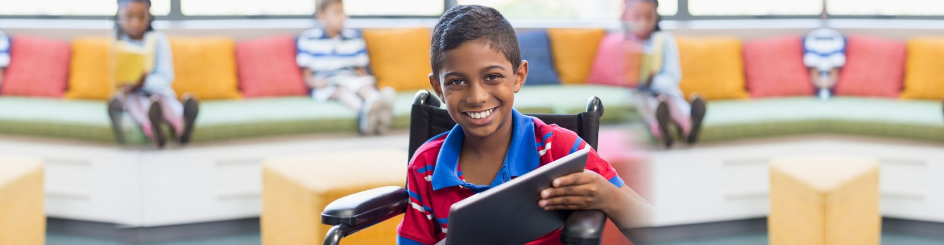 smiling boy on wheelchair using digital tablet in library at school